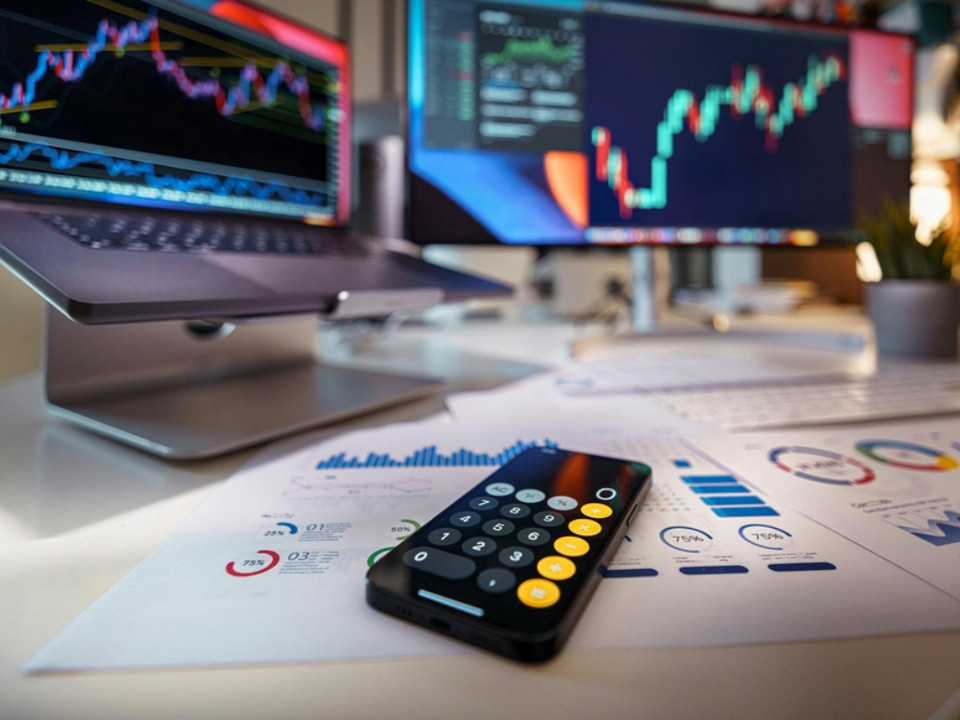 Stock trading setup: calculator on financial reports with two monitors displaying charts and graphs on the desk